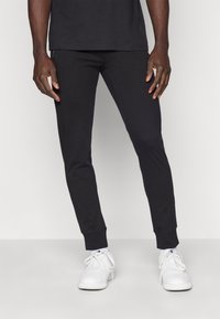 Zwarte jogginbroek van zacht materiaal, met een tapered fit, elastische tailleband en boorden. Gecombineerd met witte sneakers.