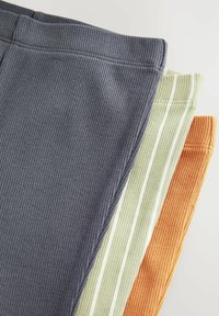 Quatre paires de pantalons en tissu côtelé de couleur gris foncé, vert clair à rayures, orange et un vert rayé. Texture douce avec des ceintures élastiques.