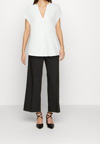 Top bianco a maniche corte con scollatura a V abbinato a pantaloni neri a gamba larga e décolleté neri a punta. Tessuto morbido, design minimalista.