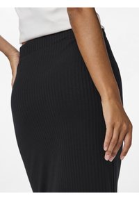 Svart ribbad kjol gjord av stretchigt tyg, med en figurnära silhuett och resårmidja. Slät yta med vertikala linjer.