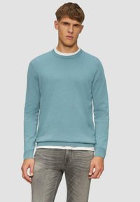 Hellblauer Rundhalspullover, gestrickte Textur, lange Ärmel, gerippte Bündchen und Saum, über einem weißen Hemd getragen, kombiniert mit grauen Jeans.