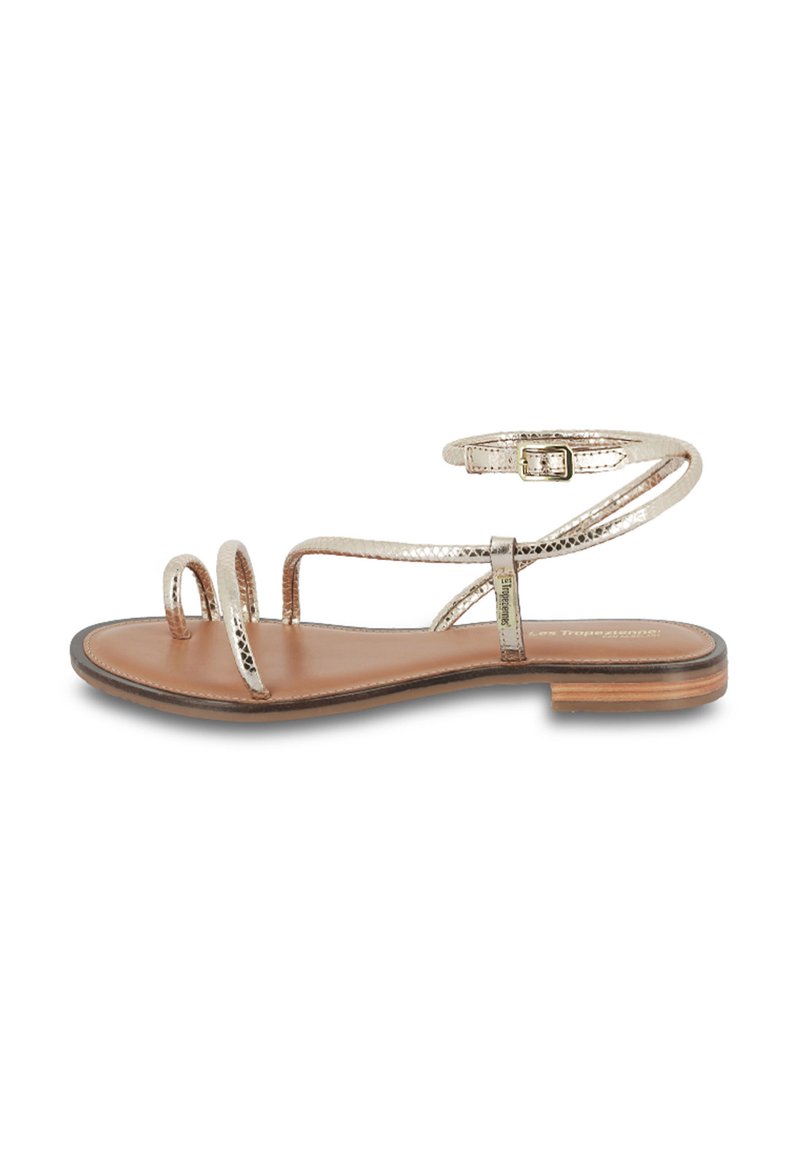 Flat sandal with metallic gold straps, open toe design, and a slim ankle buckle. Brown leather footbed and a low stacked heel.