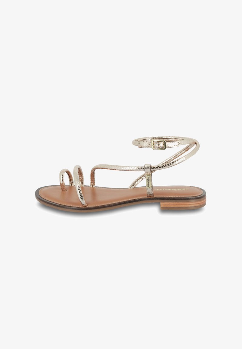 Flat sandal with metallic gold straps, open toe design, and a slim ankle buckle. Brown leather footbed and a low stacked heel.