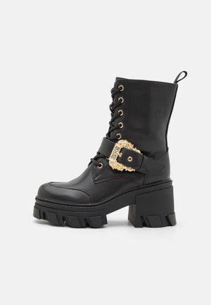 Bottes noires à lacets avec une finition brillante, plateforme épaisse, talon épais et une boucle dorée décorative sur la sangle de la cheville.
