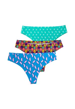 Smiling woman with blonde ponytail wearing a black bra and colorful patterned bikini bottoms standing on one leg against a plain background.