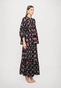 Svart blomstret kjole med pufferm, lagdelt design og fargerike rosamønstre. Kombinert med nude høye hæler.