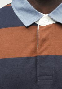 Polo särk, millel on horisontaalsed triibud pruunis, mereväesinises ja valges, kontrastse teksakaeluse ja ees oleva nööbiridadega.