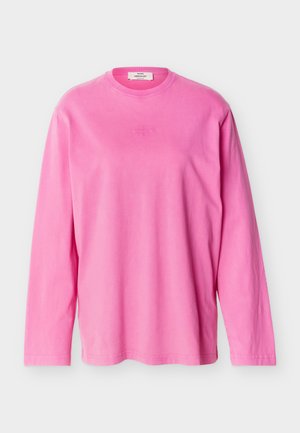 Tricou roz aprins cu mâneci lungi și guler rotund, cu un logo subtil în relief centrat pe piept și o etichetă de marcă în interiorul gulerului.