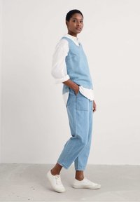 Jasnobłękitne ogrodniczki z bezrękawnikami, z bocznymi kieszeniami, nałożone na białą koszulę z guzikami, w połączeniu z białymi trampkami.