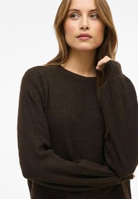 Brązowy sweter z dzianiny o teksturowanym wzorze, z prążkowanym dekoltem w serek i długimi rękawami. Miękka tkanina z luźnym krojem.