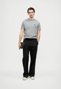 Pilkos medvilnės marškinėliai su nedideliu juodu logotipu kairėje krūtinės pusėje, derinami su juodomis pritaikytomis kelnėmis ir sportbačiais. Paprastas ir minimalus dizainas.