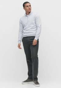 Jasnoszara bluza z suwakiem przy kołnierzu, połączona z ciemnoszarymi spodniami. Model stoi w neutralnym otoczeniu, nosząc casualowe sneakersy.