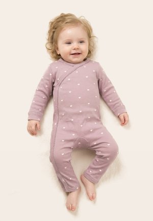 Naeratav beebi lokkis blondide juustega, seljas roosa pika varrukaga bodi valgete südame mustritega, lamab heledal pinnal.