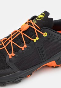 Czarne buty sportowe z pomarańczowymi i żółtymi sznurówkami, gumowymi akcentami, teksturowaną siateczką na cholewie oraz podeszwą z bieżnikiem zapewniającą przyczepność. Posiadają zapięcie z regulacją dla pewnego dopasowania.