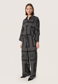 Set asortat alb-negru care include o cămașă cu mânecă lungă, colorată, cu linii geometrice și pantaloni largi cu talie ajustabilă prin șnur.