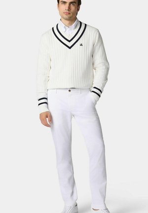 Weißer Rippstrickpullover mit marineblauen Streifen am Kragen und an den Bündchen, kombiniert mit weißen Hosen und weißen Sneakers, was einen sauberen, abgestimmten Look schafft.