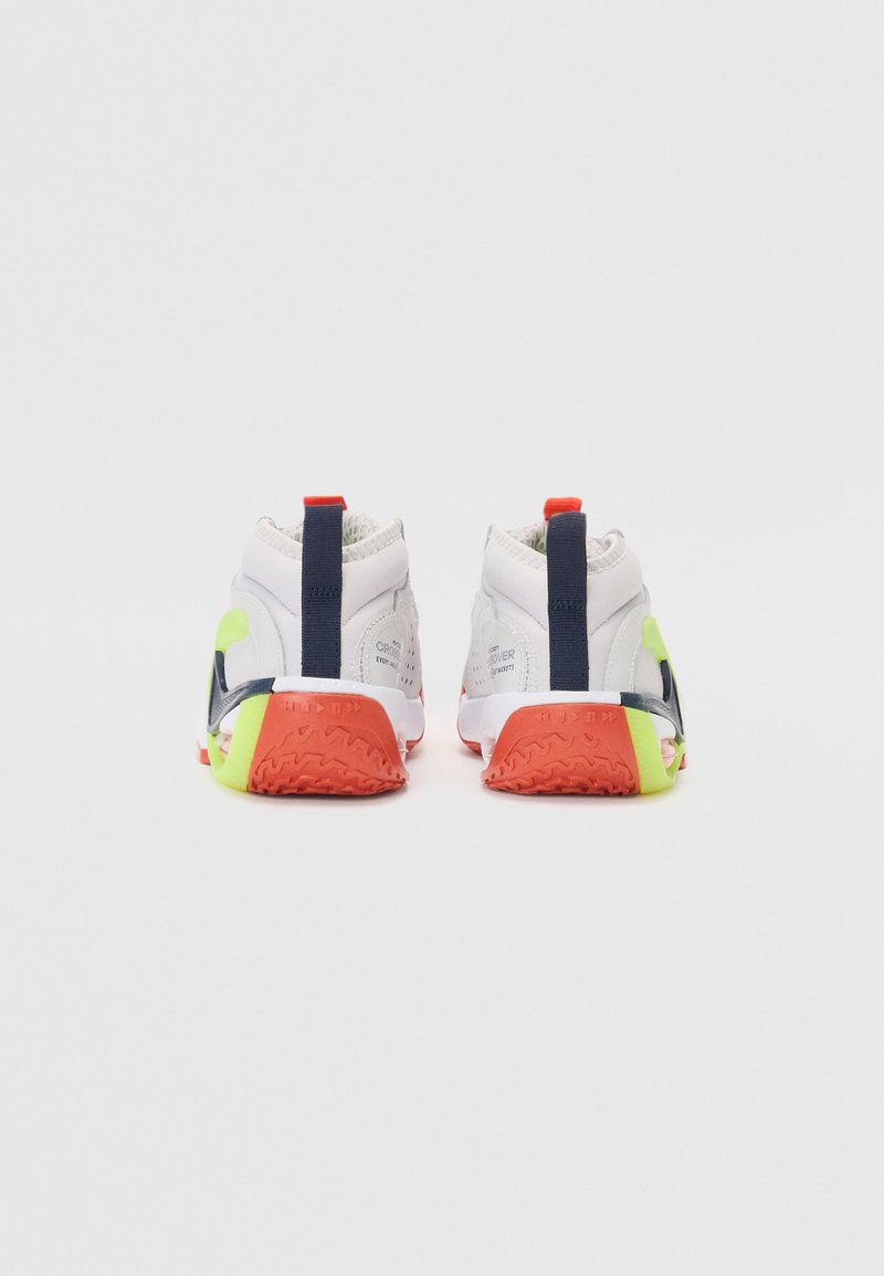 Zapatillas deportivas blancas con acentos en color marino, detalles en naranja brillante y verde, y suelas de goma texturizadas. Cuentan con un collarín acolchado y un lazo en el talón.