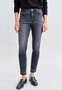 Jeans in denim nero a vita alta, skinny, con leggere sfumature, chiusura con bottone e orli grezzi. Abbinati a mocassini neri.