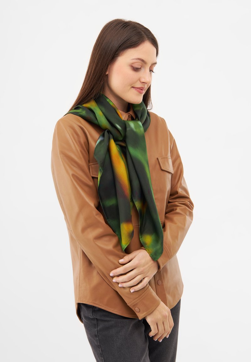 Grön och gul silkeser scarf draperad runt halsen, med en slät yta och livligt, abstrakt mönster. Bärs över en brun läderjacka.