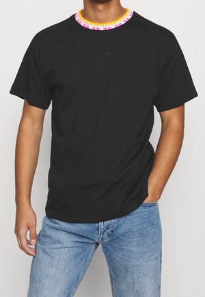 Sort T-shirt med korte ærmer, med krave i mønstrede farver i pink, hvid og gul, præget logo på brystet, båret med lyseblå jeans på model.