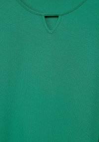 Grünes Kurzarmoberteil mit rundem Halsausschnitt und einem kleinen Schlüssel-Detail auf der Vorderseite, aus glattem, strukturiertem Stoff gefertigt.