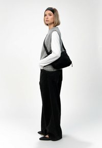 Borsa a tracolla nera con cintura regolabile, abbinata a un maglione grigio senza maniche e a una camicia bianca a maniche lunghe, insieme a dei pantaloni neri larghi.