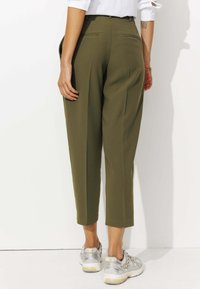 Pantalons tapered vert olive avec taille haute, poches latérales et poches passepoilées à l'arrière, associés à des baskets de sport argentées.