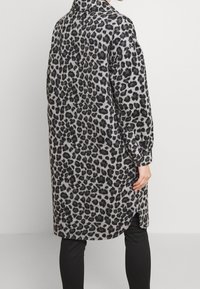 Leopardenmuster, graues Langarmshirt aus weichem Material. Mit Kragen, langen Ärmeln und seitlichen Schlitzen am Saum.