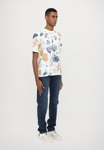 White t-shirt with a floral pattern in blue, orange, and green, paired with dark denim jeans and white sneakers.