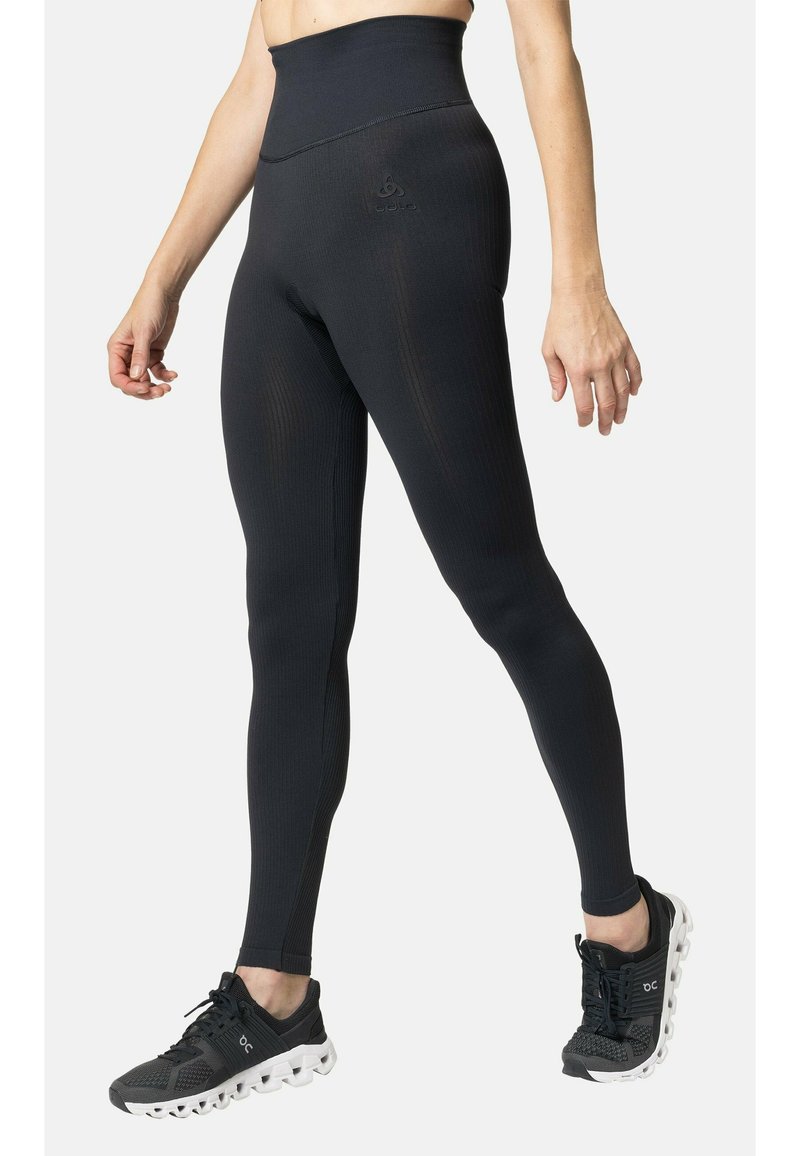 Zwart high-waisted leggings met een geribbelde textuur en logo-detail aan de voorkant, gecombineerd met zwarte sportschoenen met een golfachtige zool.