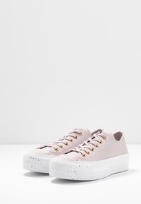 Zapatillas de deporte rosa claro hechas de material sintético con suela de plataforma, ojales dorados y una suela de goma blanca moteada.