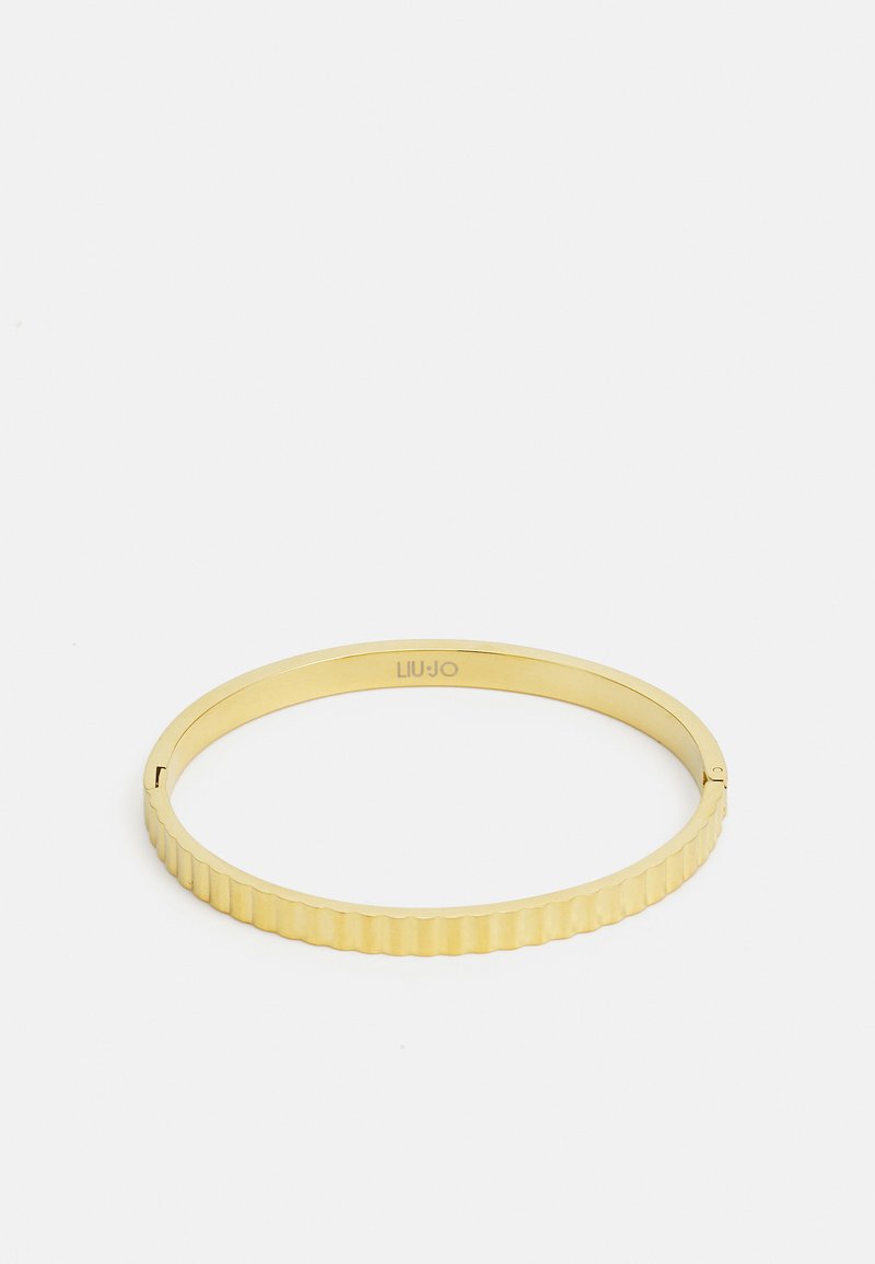 Gullfarget armring med ribbet tekstur, som har en glatt, polert innside og en liten logo gravering.