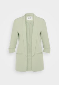 Světlý zelený blazer s klopovým límcem, zvednutými rukávy a dvěma předními kapsami. Hladká látka a na míru šitý střih. Bez knoflíků.