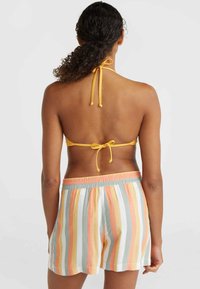 Dzeltena halter tipa bikini augšdaļa ar sasietu aizmuguri, apvienota ar gaišiem šortiem, kuru rakstā ir horizontālas svītras pasteļkrāsās: oranžā, zilā un dzeltenā.