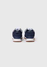 Une paire de baskets New Balance bleu marine avec des semelles intermédiaires blanches et des semelles extérieures en caoutchouc couleur gomme, vues de l'arrière sur un fond blanc uni.