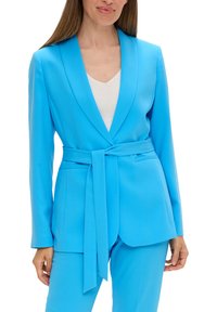 Blazer ajusté en tissu bleu vif, avec un col châle, une ceinture à la taille et deux poches latérales. Design lisse et structuré.