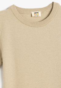 Beżowy sweter dzianinowy z okrągłym dekoltem, z fakturowaną powierzchnią. Metka wskazuje rozmiar 6-9 lat.