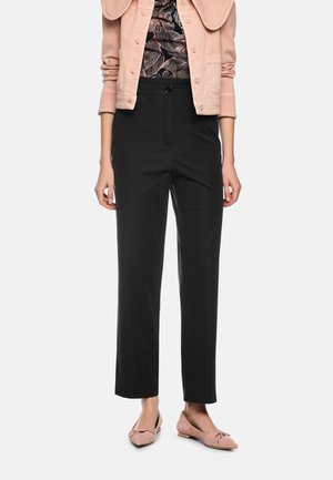 Schwarze, gerade geschnittene Hose mit glatter Textur und einem einzelnen Knopfverschluss. Kombiniert mit einer rosa Jeansjacke und weichen rosa flachen Schuhen.