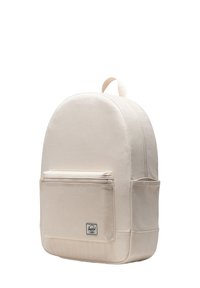 Beige canvas backpack with a rounded top, front zip pocket, and logo label at the base. Features minimalist design and textured fabric.