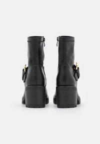 Botas de tobillo de cuero negro con punta redondeada, tacón alto en bloque y detalles en tono dorado en una correa lateral. Textura suave.