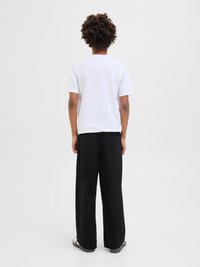 Hvit t-skjorte med korte ermer kombinert med løstsittende svarte bukser. Buksene har baklommer og en rett ben-design.