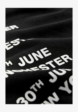 Svart bomullstyg med vit text, inklusive namn på platser och datum, med en slät yta och lätt skrynklig utseende.