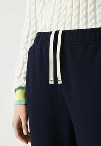 Mörkblå sweatpants med en texturerad tyg, featuring en dragsko i midjan och vita, löst flätade snören.