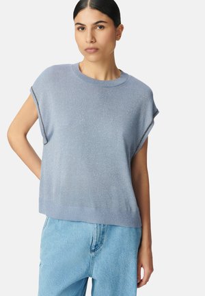 Lichtblauwe gebreide trui met een gestructureerde afwerking, korte mouwen en een geribbelde zoom. Draagt over lichtblauwe denim broek.