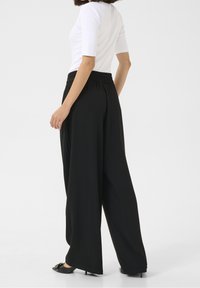 Pantalon noir à jambes larges avec taille élastique, texture lisse et design fluide, associé à un haut blanc ajusté.