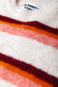 Soft knit sweater with horizontal stripes in white, pink, orange, and dark red, featuring a visible label with partially readable text.