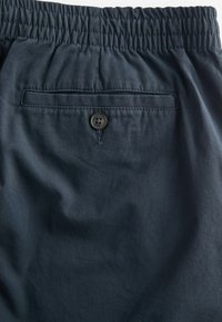 Tmavě námořnické šortky s elastickým pasem, se zadní kapsou na knoflík a hladkou texturou látky.