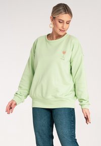 Jasnozielona bluza z okrągłym dekoltem i opuszczonymi ramionami. Zawiera haftowaną grafikę kieliszka wina oraz napis "rosé".