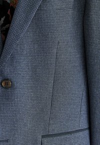 Blazer bleu texturé avec un motif subtil, fermeture à un bouton, et un col cranté avec une coupe ajustée.