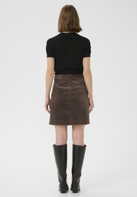 Jupe en velours côtelé marron, taille ajustée, poches arrière, associée à un haut noir à manches courtes et des bottes en cuir noir montantes.